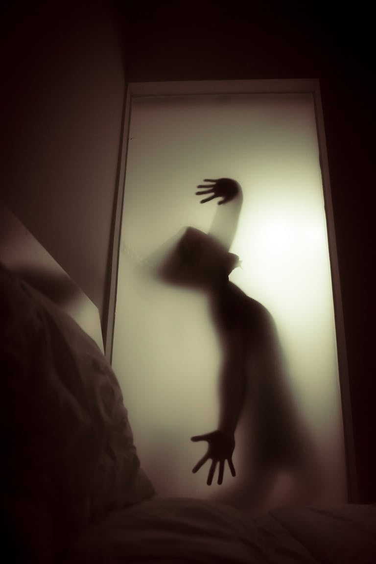 A ghostly silhouette of a person behind frosted glass, evoking a spooky and mysterious atmosphere.