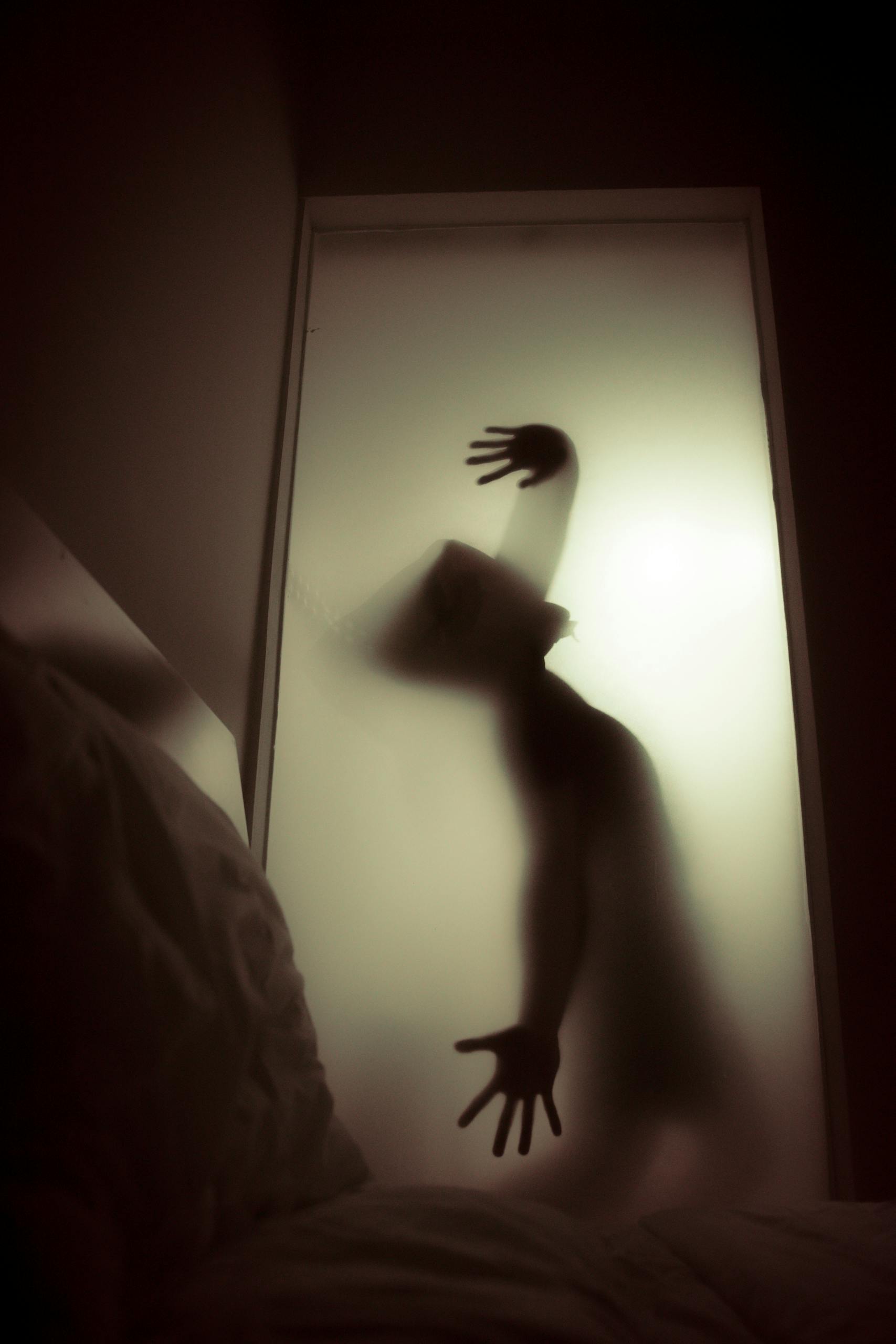A ghostly silhouette of a person behind frosted glass, evoking a spooky and mysterious atmosphere.