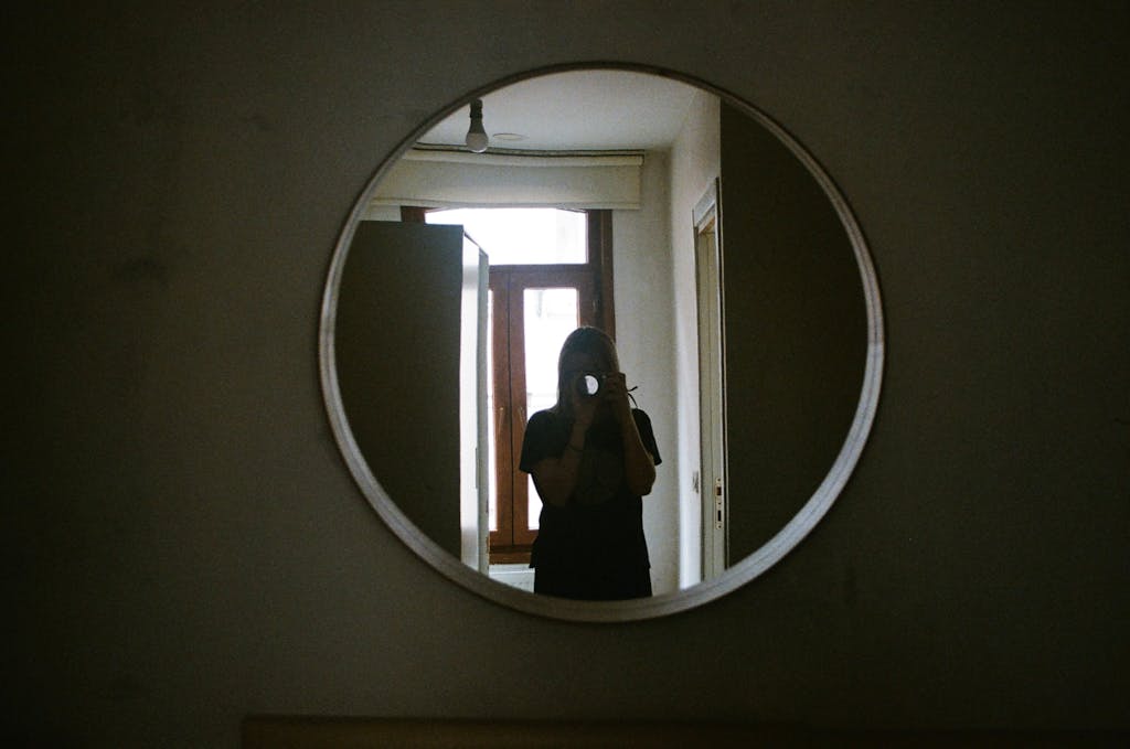 A person taking a photo through a circular mirror in an indoor setting.