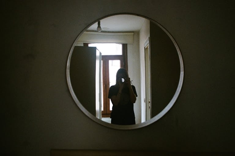A person taking a photo through a circular mirror in an indoor setting.