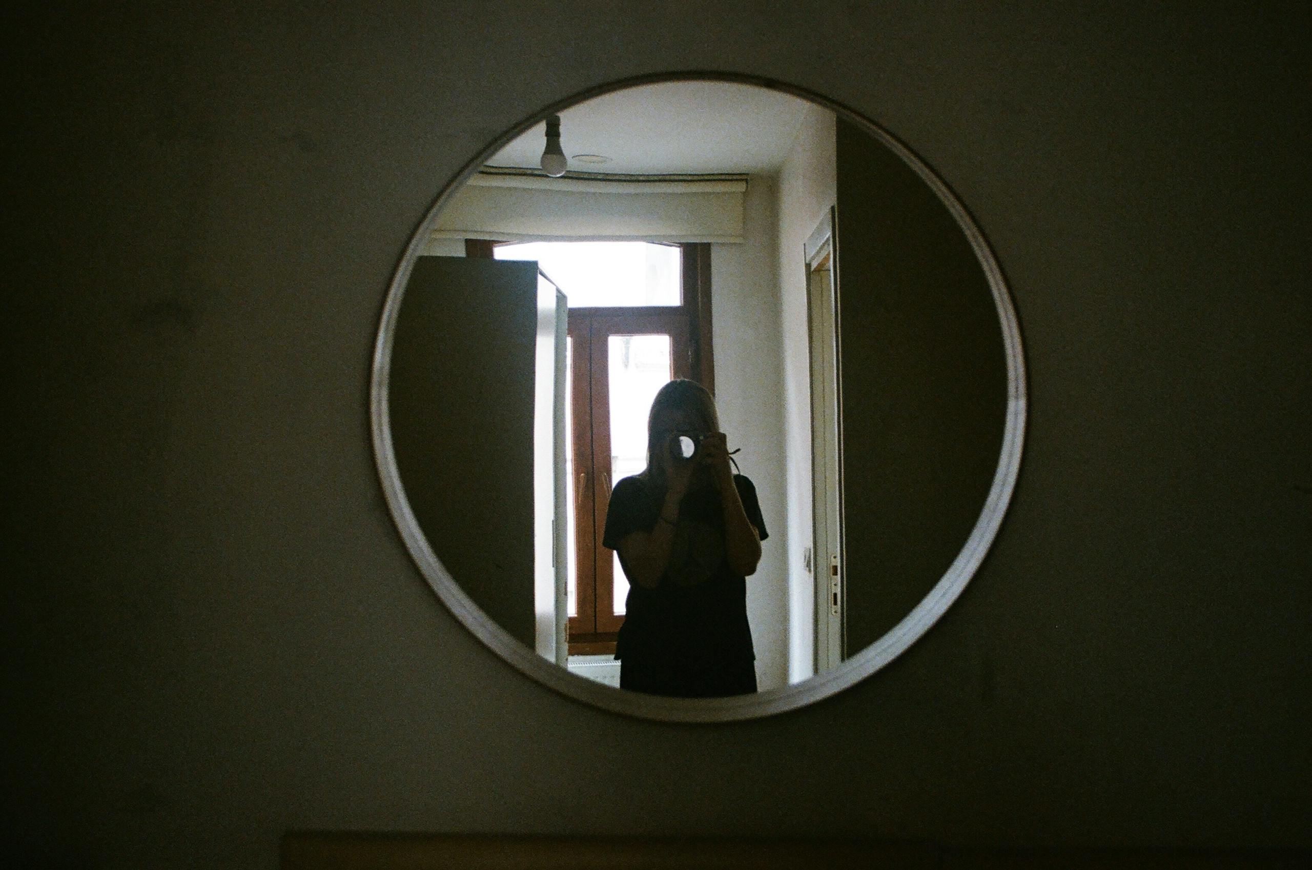 A person taking a photo through a circular mirror in an indoor setting.