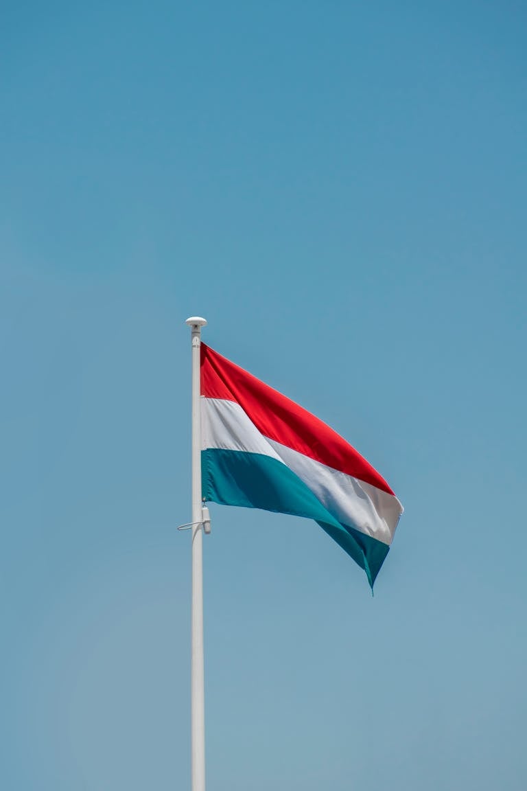 Luxembourg's national flag waving under a clear blue sky in Amsterdam, Netherlands.