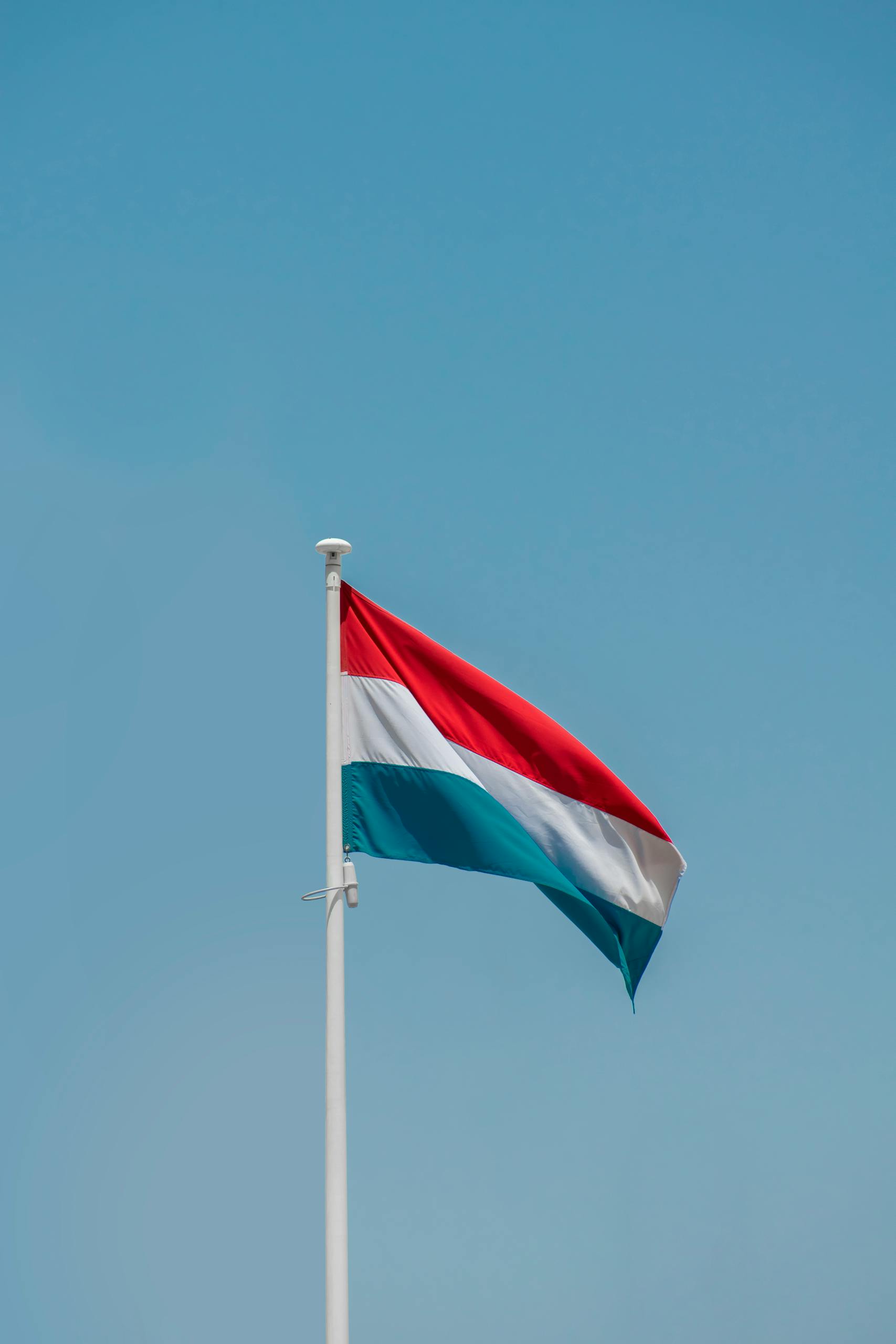 Luxembourg's national flag waving under a clear blue sky in Amsterdam, Netherlands.
