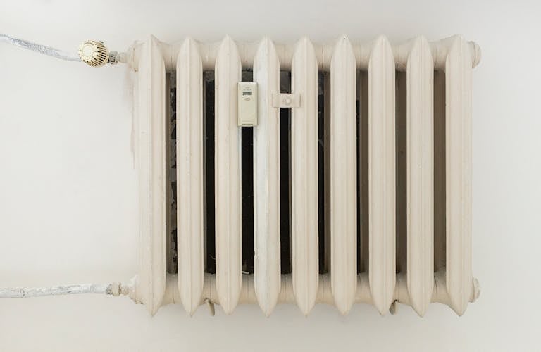 A classic white metal radiator on a plain wall, showcasing minimalist interior design.