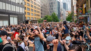 A large crowd of diverse protesters raising fists in a city street during daytime.