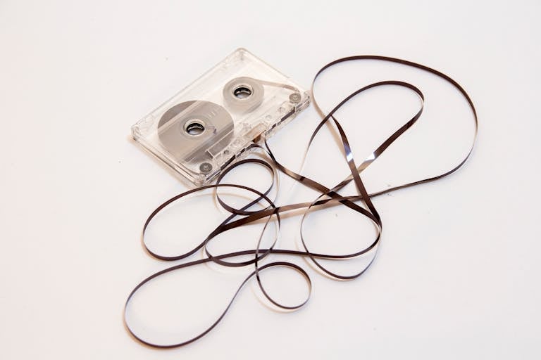 A nostalgic image of a vintage cassette tape with its magnetic ribbon artistically tangled on a plain background.