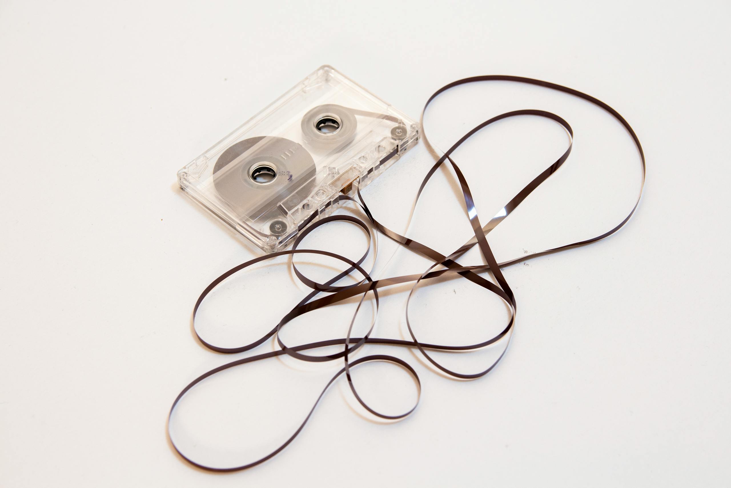 A nostalgic image of a vintage cassette tape with its magnetic ribbon artistically tangled on a plain background.