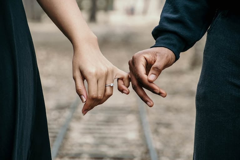 A romantic couple holding hands, symbolizing love and unity on a scenic railtrack.