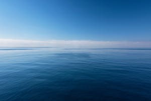 A serene ocean view with a clear blue sky and calm waters, evoking peace and tranquility.