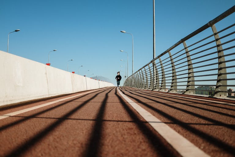 A solitary runner on a deserted bridge, showcasing urban architecture and shadows.