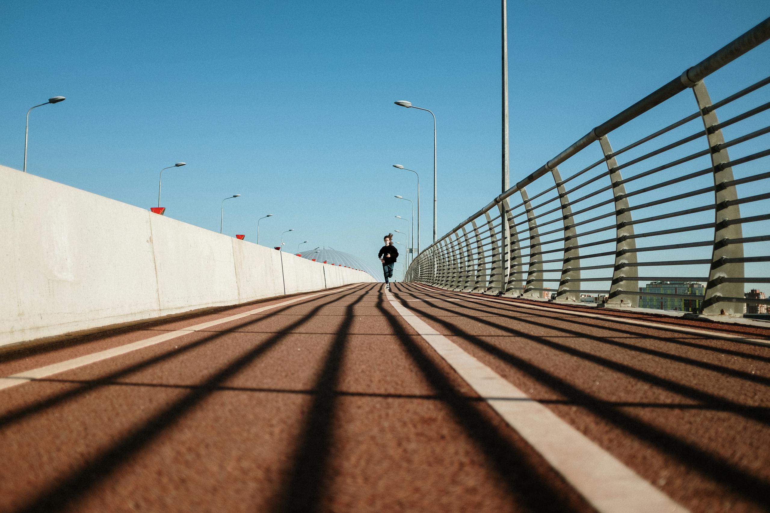 A solitary runner on a deserted bridge, showcasing urban architecture and shadows.