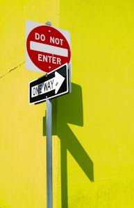 A vibrant yellow wall featuring a 'Do Not Enter' and 'One Way' sign casting shadows.