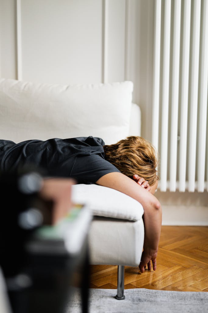 A young adult lying face down on a white sofa indoors next to a radiator, showcasing a relaxed setting.
