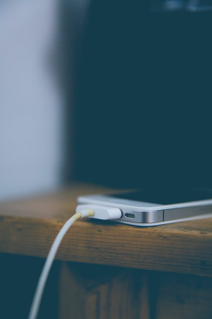 Close-up of a smartphone charging on a wooden desk, showcasing technology in an office setting.