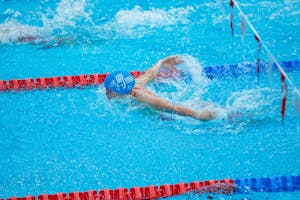 Swimmer in blue cap mid-butterfly stroke in indoor pool with red lane markers.