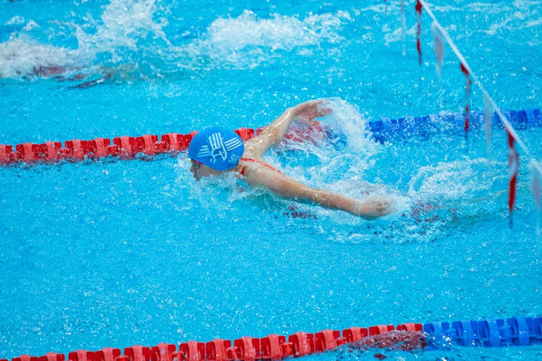 Swimmer in blue cap mid-butterfly stroke in indoor pool with red lane markers.