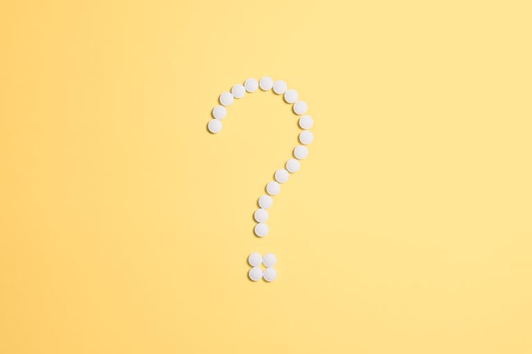White pills arranged into a question mark shape on a vibrant yellow background.