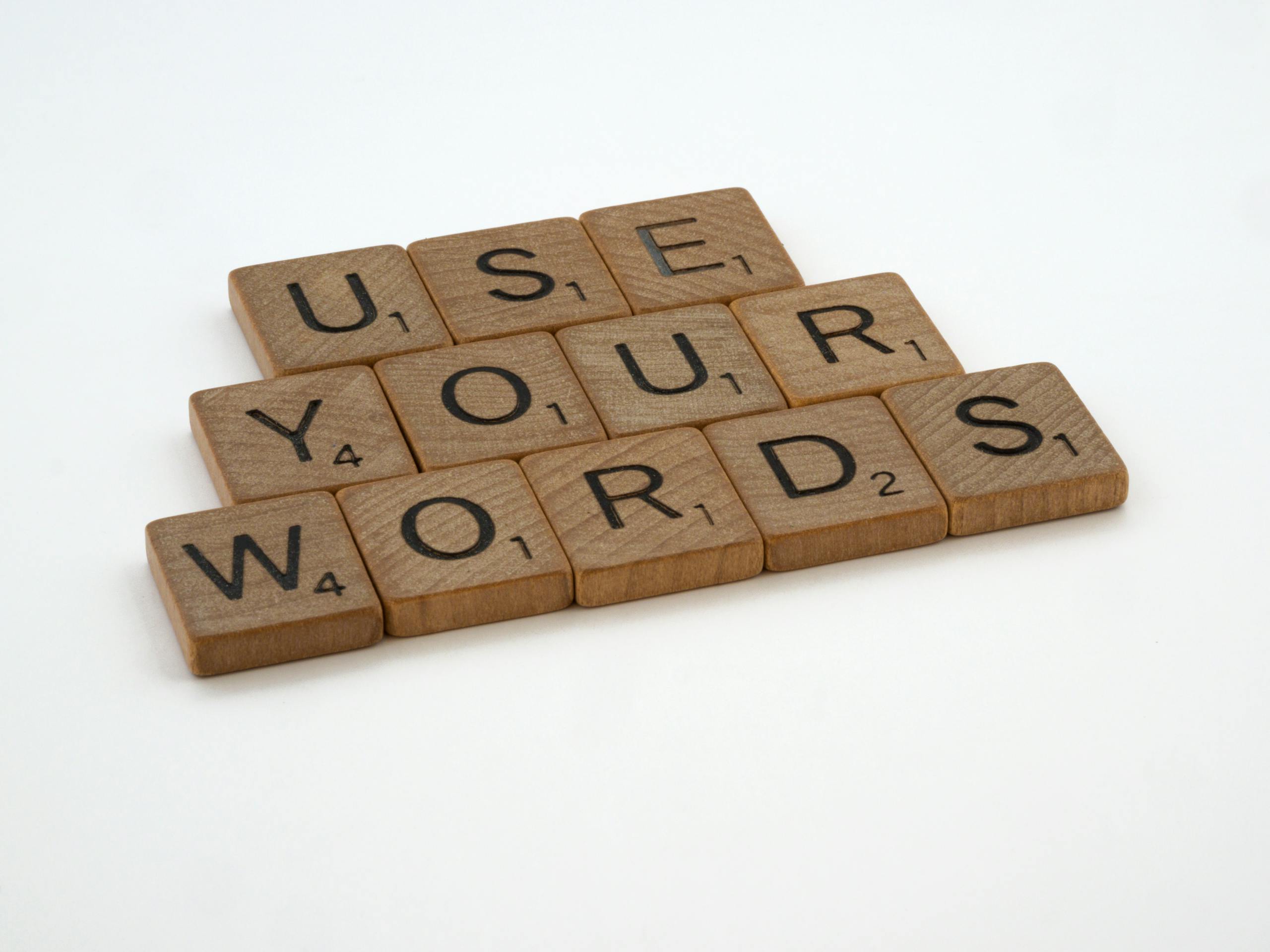 Wooden letter tiles spell 'USE YOUR WORDS' on a white background, promoting linguistic creativity.