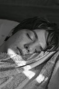 Young adult sleeping peacefully under soft light, wrapped in a cozy blanket.