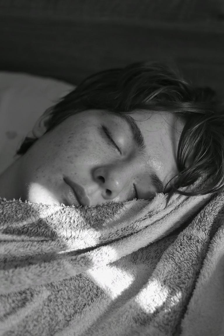 Young adult sleeping peacefully under soft light, wrapped in a cozy blanket.