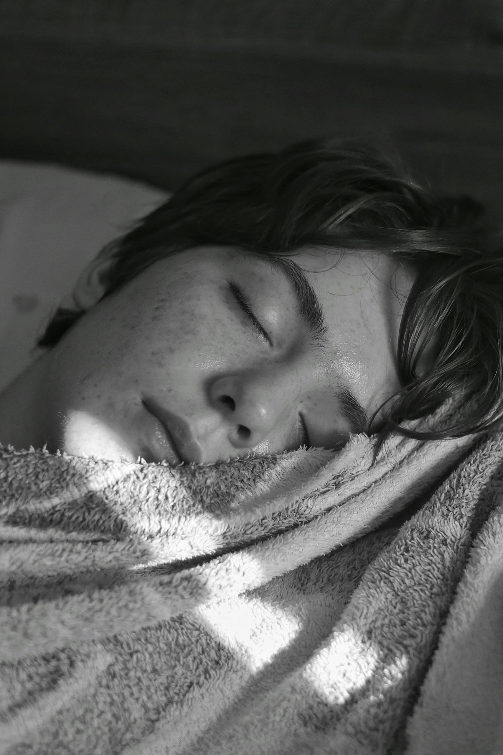 Young adult sleeping peacefully under soft light, wrapped in a cozy blanket.