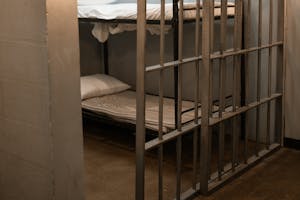 A prison cell featuring a metal bunk bed and striped sheets.