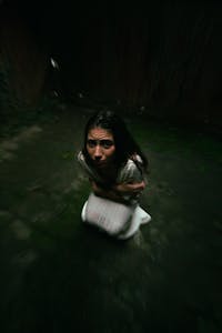 A woman appears frightened and uneasy in a dark, confined space.