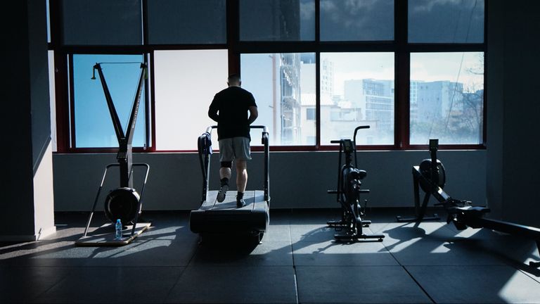 A man exercises on a treadmill in a modern gym overlooking a city skyline.