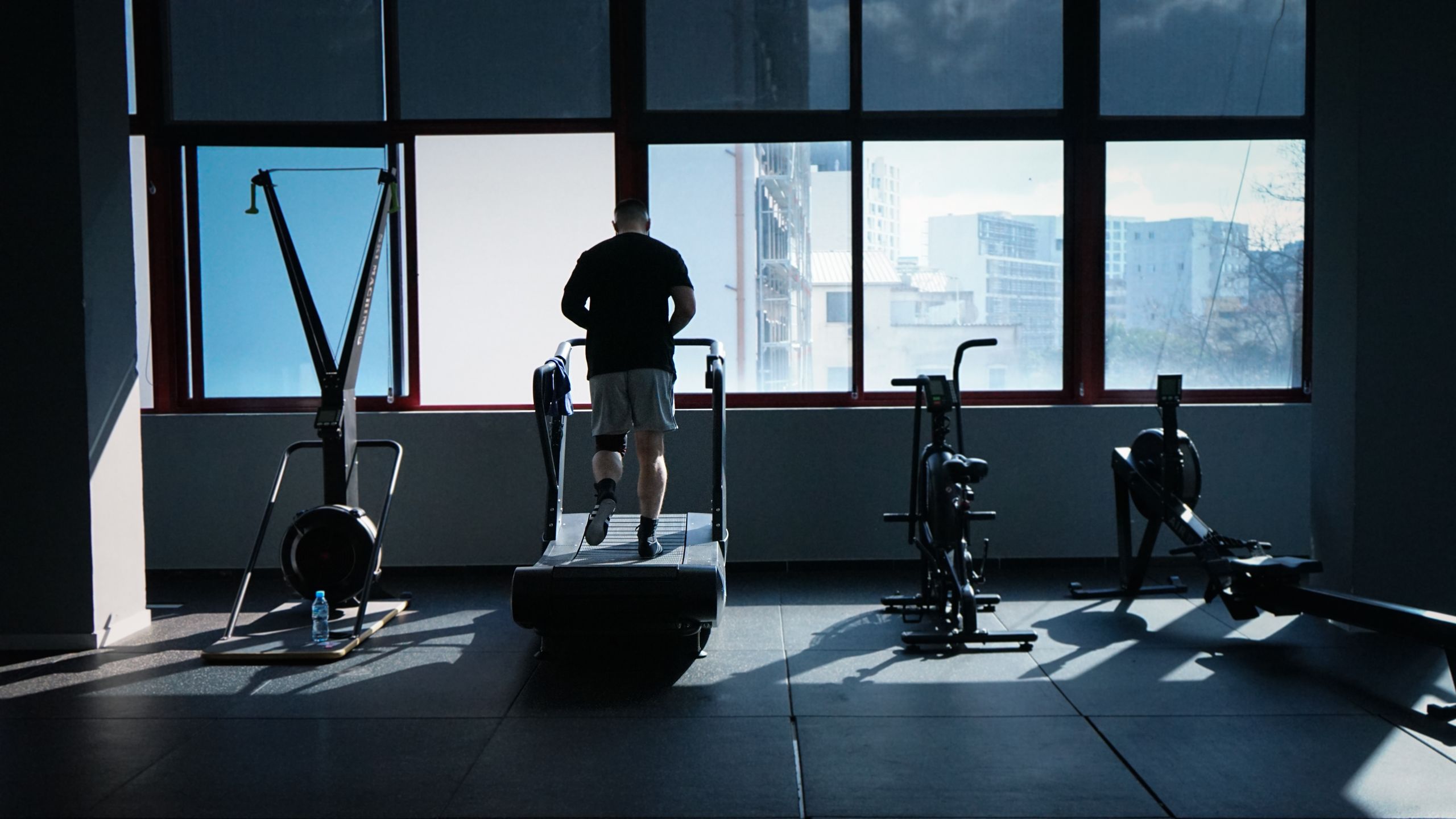 A man exercises on a treadmill in a modern gym overlooking a city skyline.